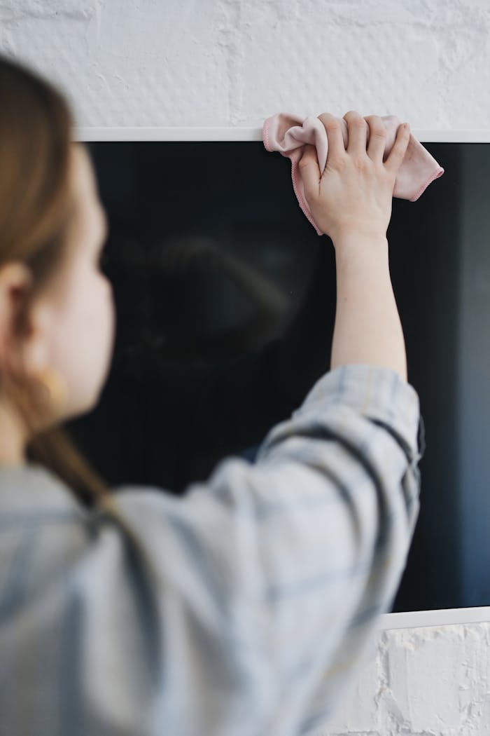Close-up of a woman cleaning a TV screen with a cloth, focusing on housework details.